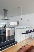 Modern, upholstered bar stools at minimalist breakfast bar in open-plan designer kitchen