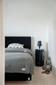 Blick in Schlafzimmer auf Doppelbett mit schwarzem Kopfteil, graue Bettwäsche, seitlich schwarzes, zylindrisches Nachtkästchen