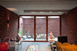 Child's bedroom with brick walls, glass wall and view of stacked firewood in foyer