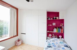 Child's bedroom with bed against hot pink shelves and next to white fitted wardrobe