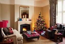 Geschmückter Weihnachtsbaum in viktorianischem Wohnzimmer mit gemütlichen Polstermöbeln vor Kaminfeuer