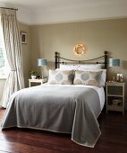 Elegant traditional bedroom; double bed with metal frame and grey bedspread below fairy light wreath on grey-painted wall