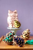 Pine cones wrapped in colourful thread in front of owl ornament