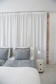 White bedroom with grey bed linen on double bed and floor-length curtains at head