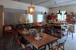 Grosszügige Küche mit Essplatz im Vintagestil, im Hintergrund Kücheninsel unter Pendelleuchten und Buffettisch unter moderner Edelstahlverkleidung