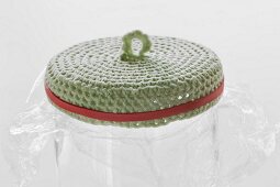 Crocheted lid soaked in glue and fixed onto glass jar covered in cling film with rubber band for shaping