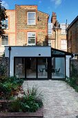 Garden of traditional, English terraced house with paved area and view of white modern extension