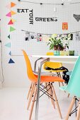 Table and colourful shell chairs in front of decorations hung on perforated wall panel