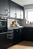 Black L-shaped kitchen units with window and serving hatch