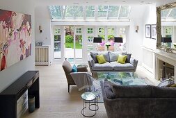 Grey sofa set and open fireplace in living room with terrace doors and glass roof