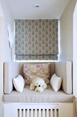 Cushions and soft toys on comfortable seat in dormer window seat with patterned Roman blind
