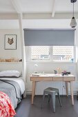Wooden desk and classic grey metal stool below window with roller blind in Scandinavian-style, teenager's bedroom