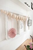 String of wooden beads and pink paper pendant on white wooden frame