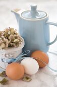 Hen's eggs with a ribbon, a hydrangea and a blue coffee pot on a marble surface