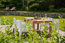 Wooden table and white, modern outdoor chairs on sunny terrace