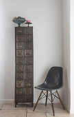 Dunkelgrauer Klassiker-Schalenstuhl neben schmalem, hohem Vintage Metallschrank in Zimmerecke