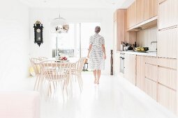 Küche mit glänzendem, weißem Boden und Frau zwischen Essplatz und Küchenzeile