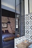 Badezimmerecke mit Ornamentfliesen und Blick in Schlafraum auf Doppelbett