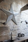 Sink in kitchen counter below metal star between retro sconce lamps on rustic stone wall
