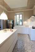 Pendant lamp above white kitchen counter and L-shaped counter in background in traditional interior