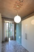 Spherical lamp suspended from painted ceiling above modern fitted cupboards with white glossy doors and glass sliding elements in traditional interior