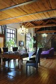 Antique dining table and black leather chairs in front of purple sofa in loft apartment