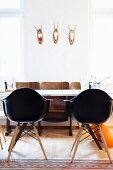 Schwarze Schalenstühle an weißem Tisch mit Retro-Kinostühlen unter drei Jagdtrophäen an Wand