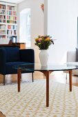 White vase of flowers on coffee table with glass top in front of dark blue armchair