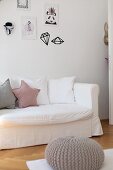 Row of scatter cushions on sofa with white loose cover below framed drawings and wall stickers