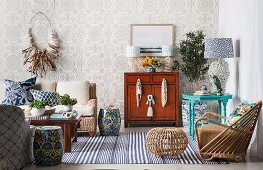 Living space with a maritime flair; Wicker armchairs and footstools, folkloric side tables and beige pattern wallpaper
