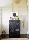 Black chest of drawers labeled with chalk against a wood-paneled wall