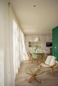 Loungebreich mit 'Shell Chair' und Glastisch, Blick auf Essbereich mit mintfarbenen Klassikerstühlen und auf weiße Designer-Einbauküche