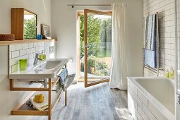 Waschtisch mit Holz Untergestell und offene Glastür mit Gartenblick in hellem, modernem Bad