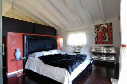 Bedroom with red partition behind bed headboard, silver chest of drawers and modern painting