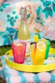 Summer drinks in colourful glasses and bottle on tray