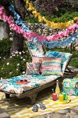 Lounger and cushions below garlands in colourful seating area in garden