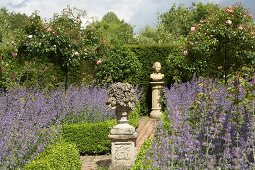 Gartenskulpturen auf Steinsäulen an Gartenweg zwischen Lavendelbeeten mit Buchshecken und Rosenbäumchen