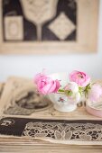 Pink ranunculus in bowl on stack of old yellowed magazines