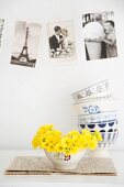 Bowl of primroses below vintage-style postcards on wall