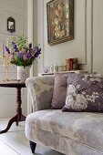 Floral scatter cushions on floral sofa in front of vase of flowers and floral painting