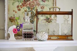 Geschliffene Glaskaraffen im Flaschenträger aus Holz vor antikem Blumenbild