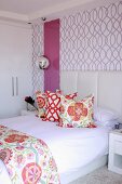 Bed with upholstered headboard and colourful scatter cushions against purple-patterned wallpaper