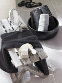 Holzbänkchen im Badezimmer mit Kosmetikspiegel, schwarze Schale mit gerollten Handtüchern