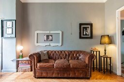 Vintage leather sofa below picture frames on grey-painted wall and table lamps on small side tables