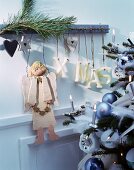 Wooden Christmas angel and letters spelling XMAS hung from rustic coat rack next to Christmas tree decorated in pastel blue