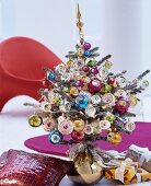 Small Christmas tree lavishly decorated with colourful baubles standing in gold vase