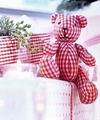 Teddybär aus rot-weiss kariertem Stoff auf Geschenken arrangiert