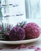 Two balls of fabric flowers and pine sprigs on dish