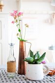 Pink aquilegia flowers in copper vase, candle in glass bottle and succulent planted in rustic mug
