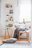 Comfortable white sofa with loose cover, scatter cushions and blanket next to books on floating shelves; Scandinavian ambiance